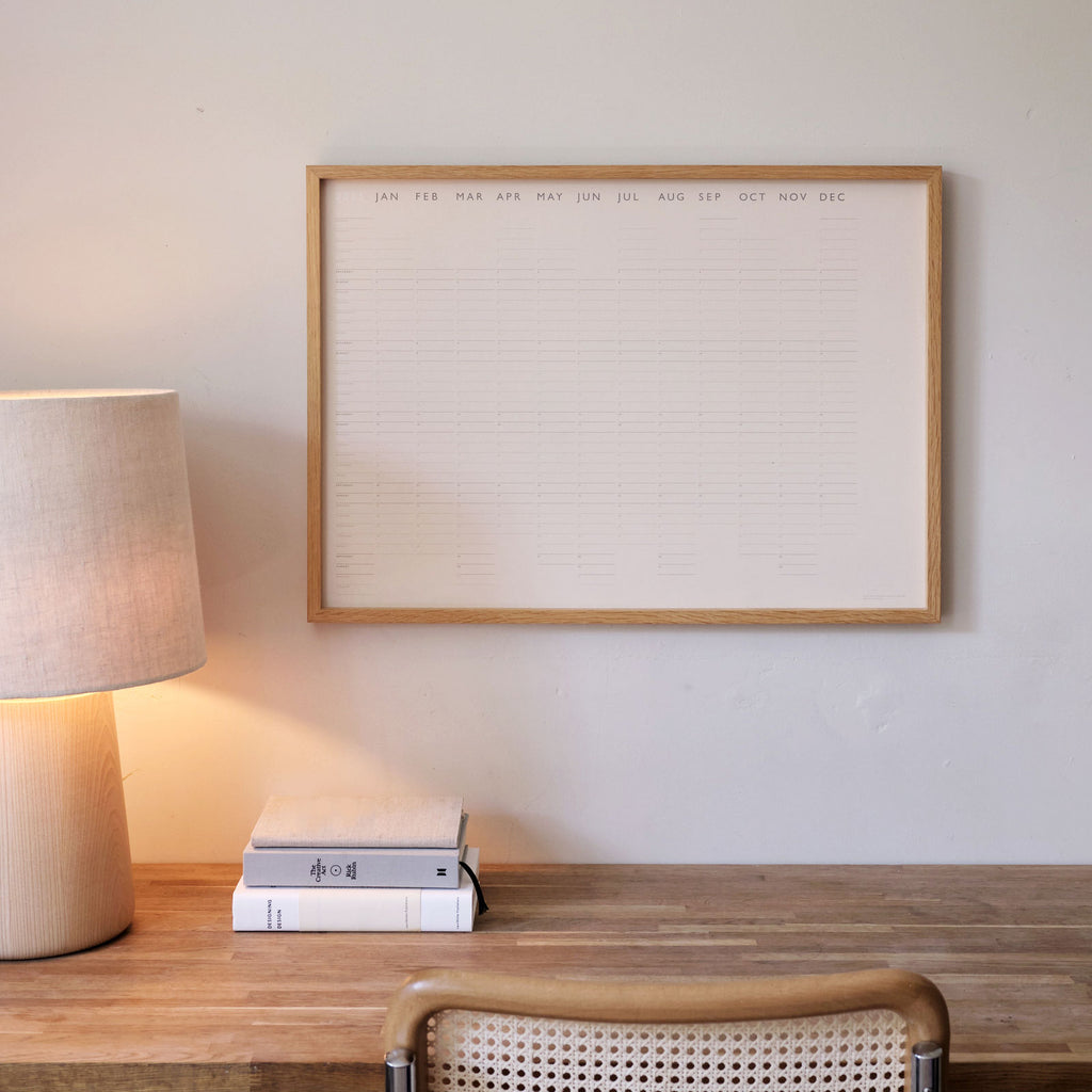 Wall Planner poster in oak frame, above oak wooden desk with Another countrty slow lamp, books, and cArne Jacobsen chair 