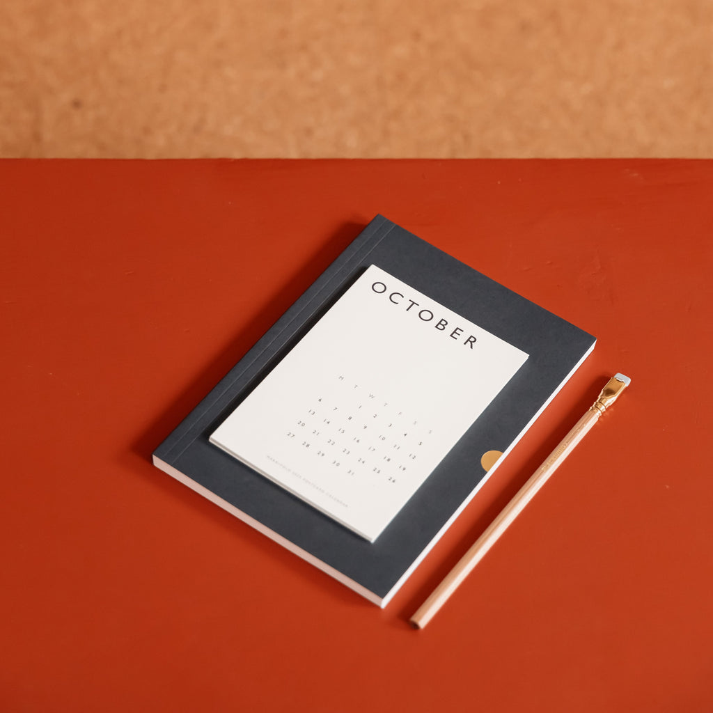 October postcard on notebook with pencil on rust red table