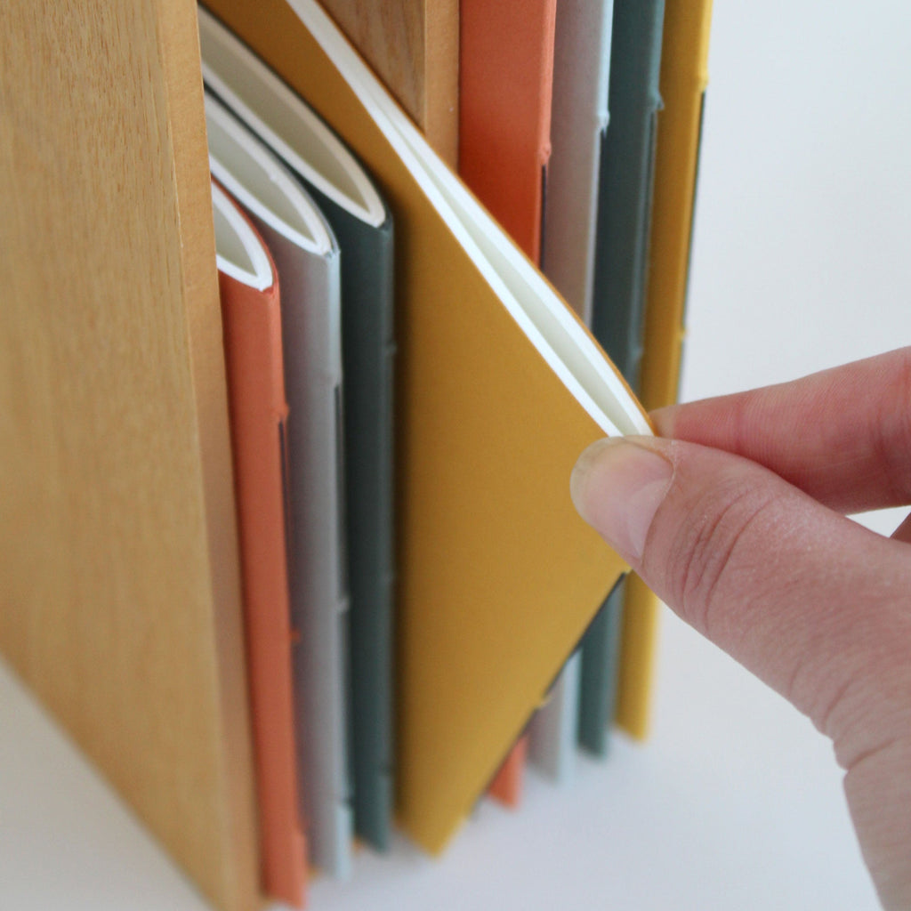 Hand taking a slim notebook from a wooden shelf with colorful notebooks.