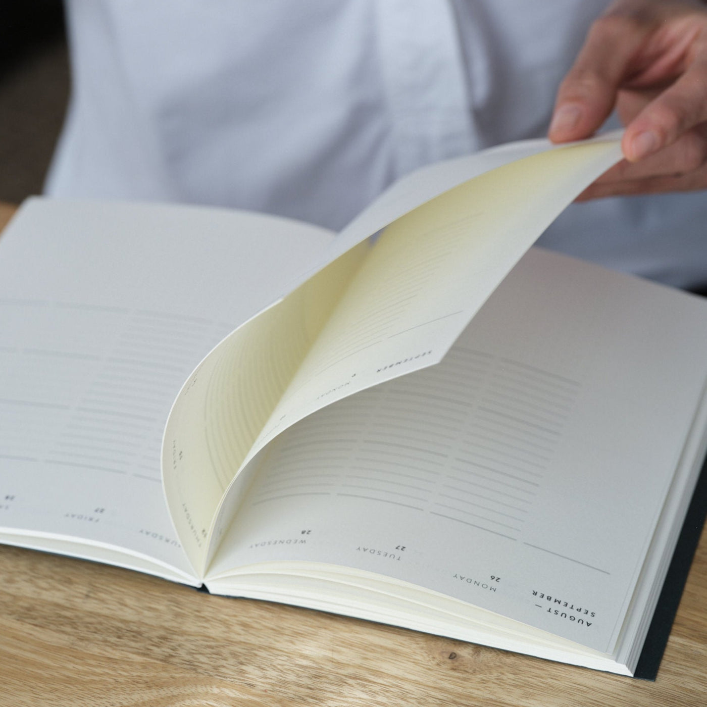 Open 2026 Diary planner on olive wood desk, with a woman wearing a white shirt flicking through the pages.