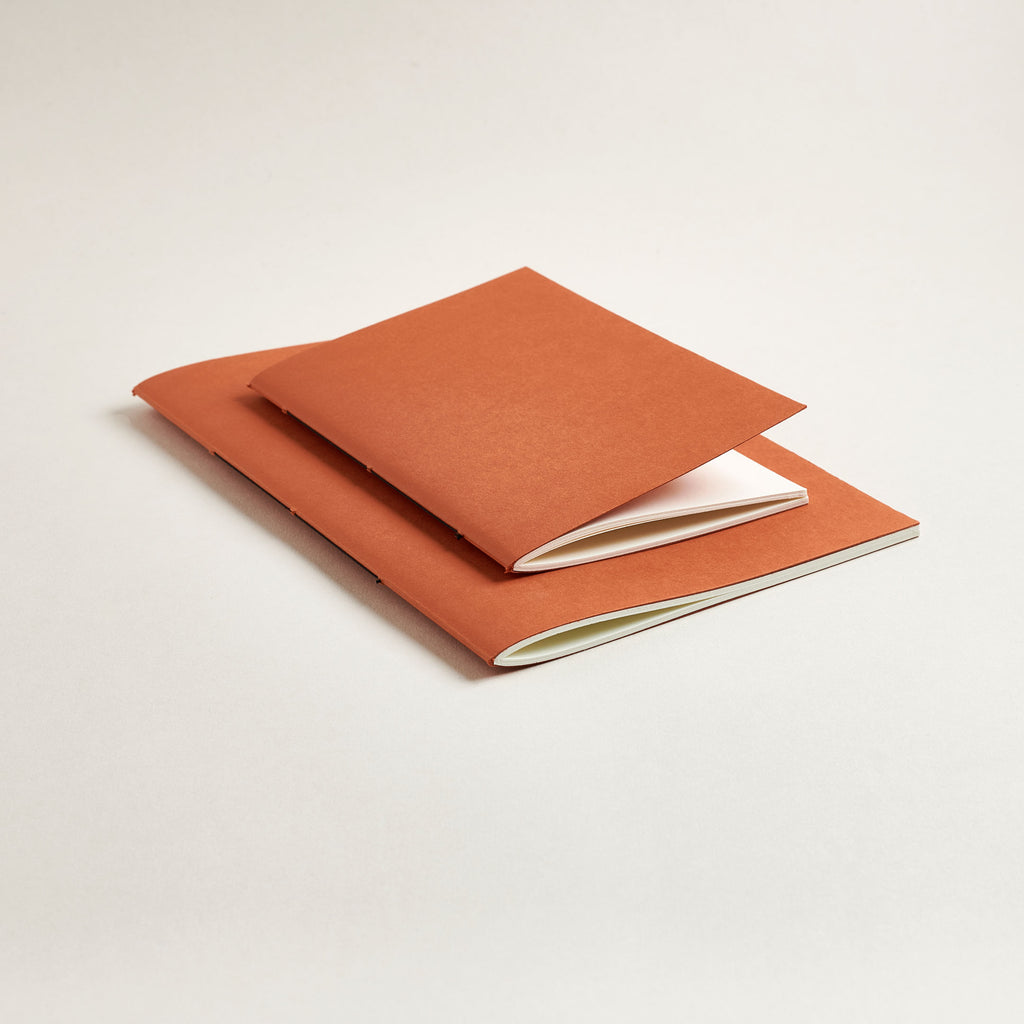 Two rust red notebooks on a light beige background