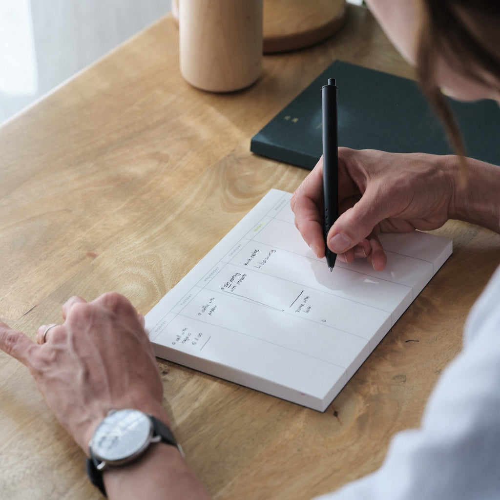Woman writing on a week planner pad, on a wooden desk
