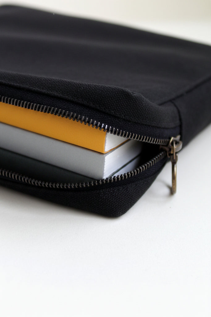 Black canvas zipper pouch with notebooks inside on a white background