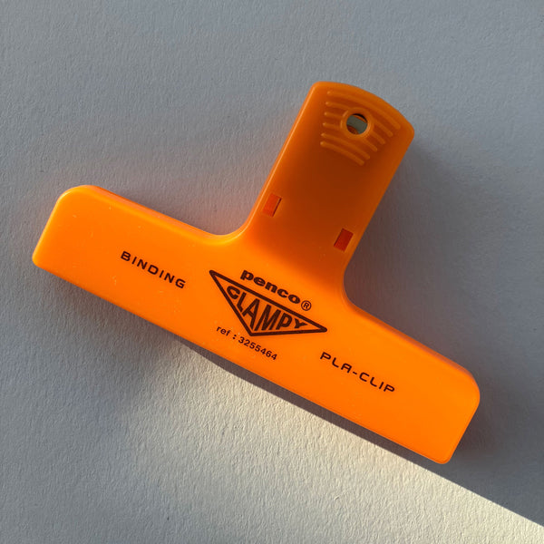 Orange binding clamp with 'Penco' branding on a gray background