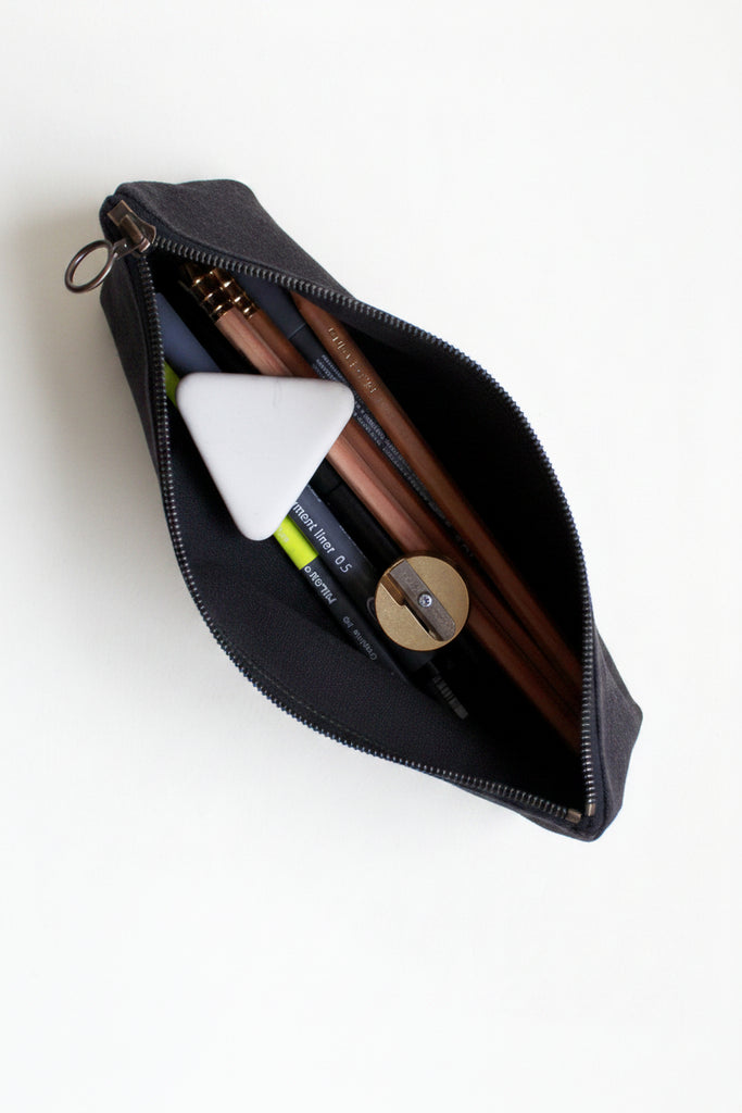 Open black canvas pencil case with stationery items on a white background