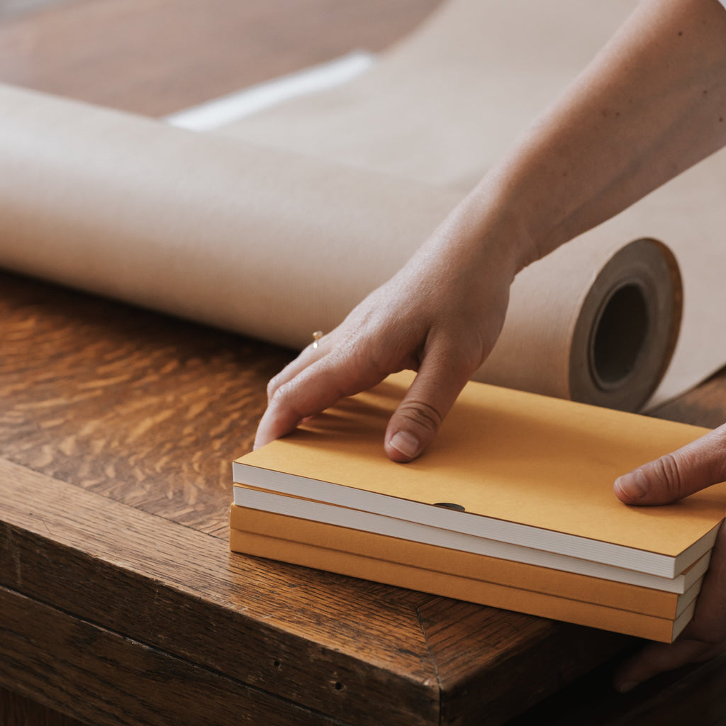 stack of mustard diaries being hand-wrapped in kraft paper amy cooper-wright